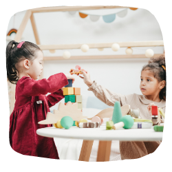 2 Mädchen sitzen am Tisch und spielen zusammen mit Klötzen.