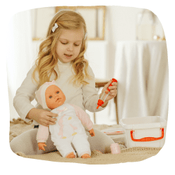 Ein Mädchen sitzt und spielt mit einer Puppe und einem Arztkoffer.